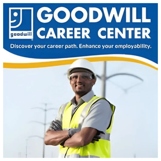 A man in a safety vest and hard hat stands with arms crossed under a sign reading “Goodwill Career Center—Discover your career path. Enhance your employability.”.
