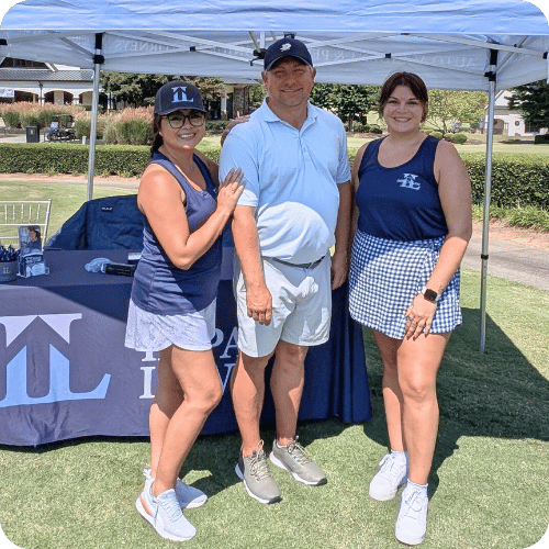Three people pose and smile in front of a booth under a canopy tent at an outdoor event, dressed in athletic wear.