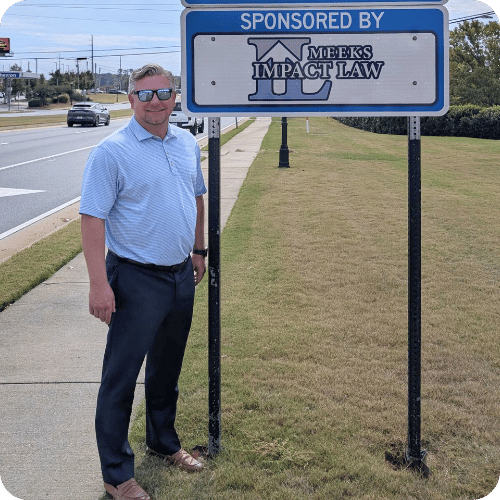 A man in sunglasses stands on a sidewalk next to a sign that reads “Sponsored by Meeks Impact Law.”.