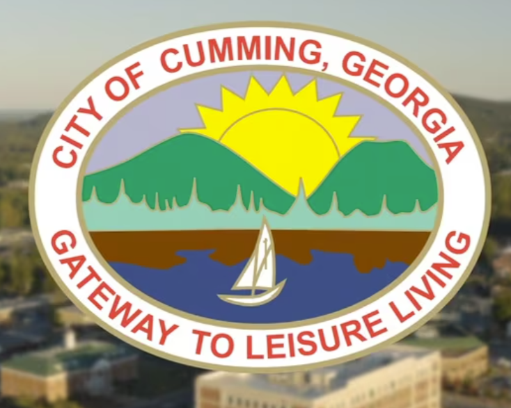 Seal of the City of Cumming, Georgia, showing a sun over green hills, a lake with a sailboat, and the text “Gateway to Leisure Living.”.