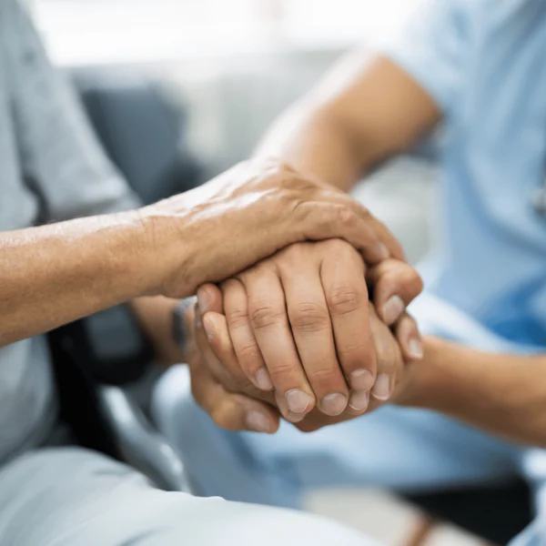 A healthcare worker holds the hands of an older adult, providing comfort and support in a medical or caregiving setting.