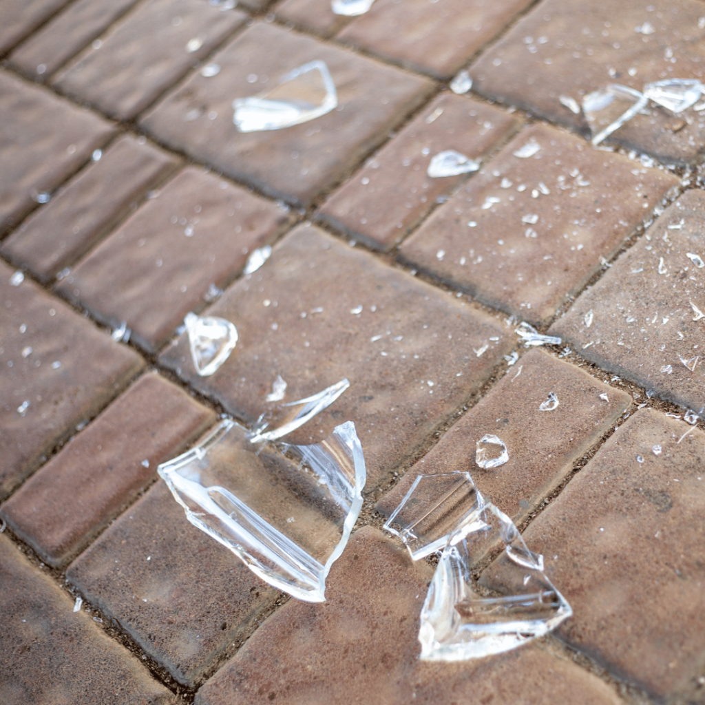 Broken glass pieces scattered on a red brick pavement.