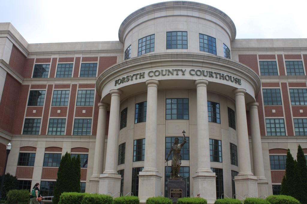 The front entrance of Forsyth County Courthouse, with a statue of Lady Justice and large columns, is shown on a cloudy day.