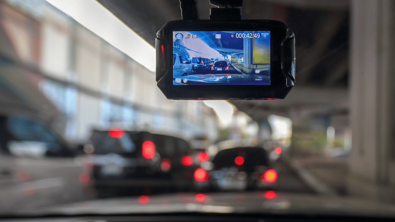 Dashboard camera shows a recording of heavy traffic under an overpass, with several vehicles stopped ahead and blurred surroundings visible through the windshield.