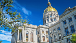 The image shows a large historic building with a gold dome, white stone walls, and arched windows, set against a clear blue sky.
