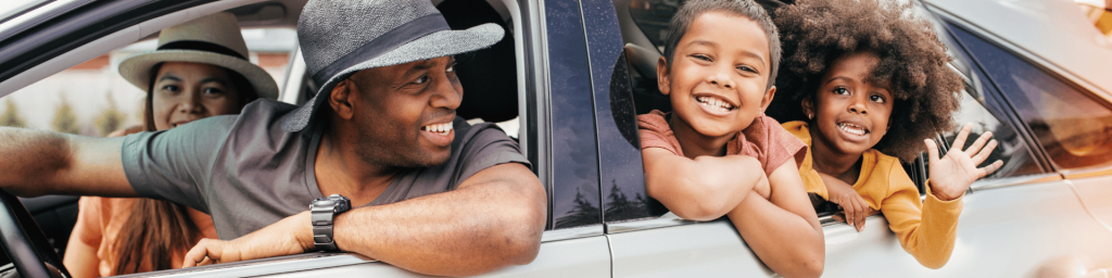 A family of four sits in a car with two kids leaning out the window, smiling and waving, while two adults look on from the front seats.