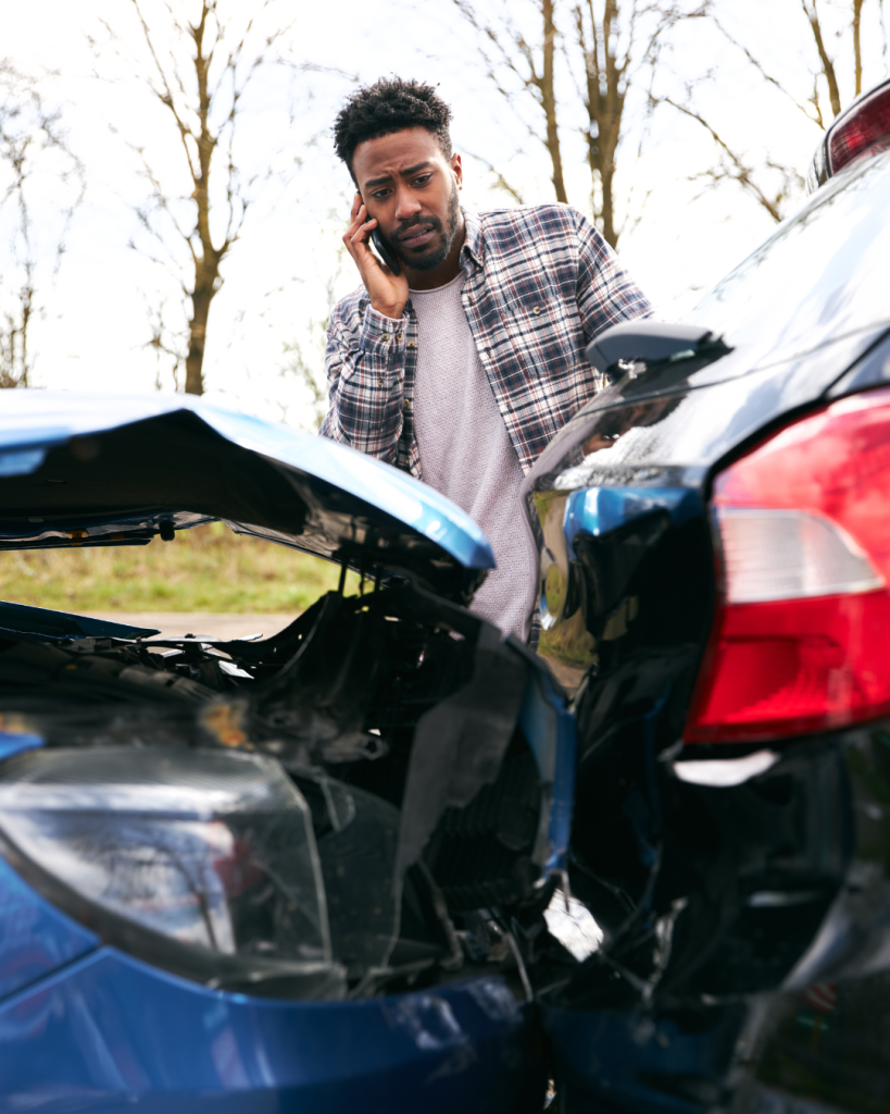 A man stands by two cars involved in a rear-end collision, talking on his phone with a concerned expression. The cars have visible damage.